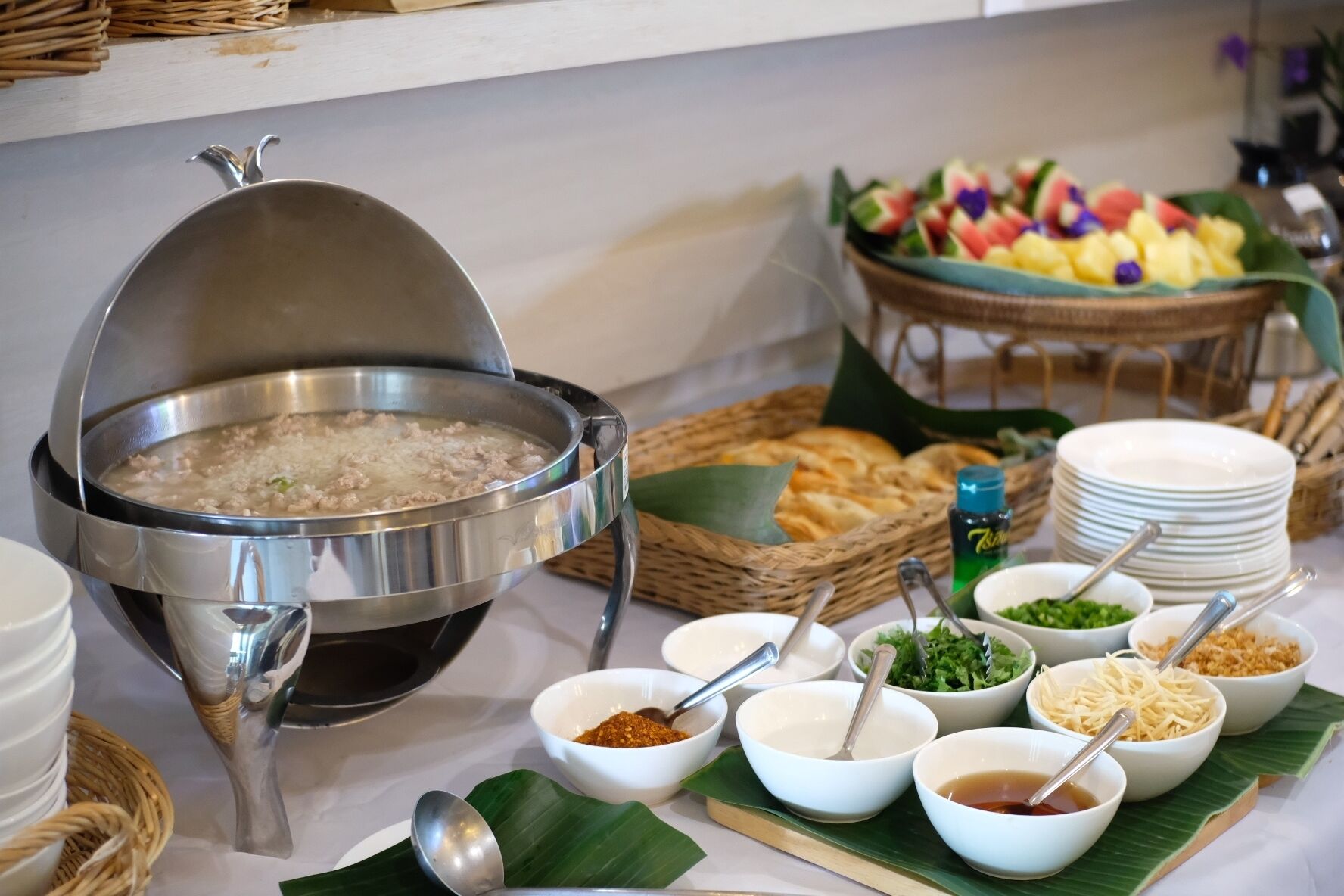 A buffet setup with a large pot of soup, various side dishes, and a fruit display.
