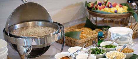 A buffet setup with a large pot of soup, various side dishes, and a fruit display.