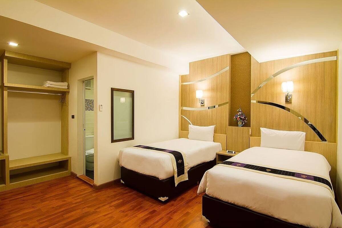A hotel room with two beds, a wooden wardrobe, a mirror, and a small table.