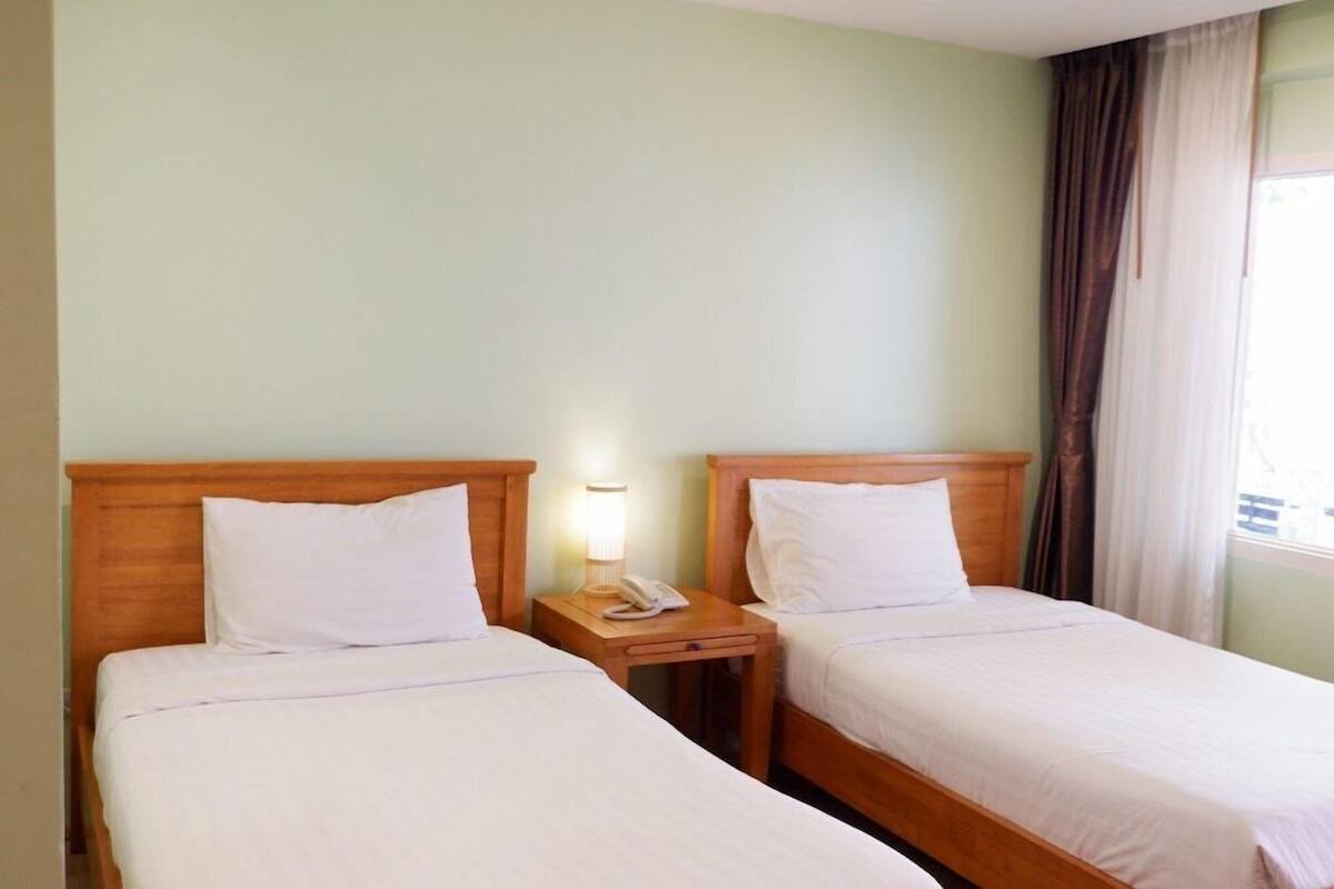 A hotel room with two single beds, a nightstand with a lamp, and a window with curtains.