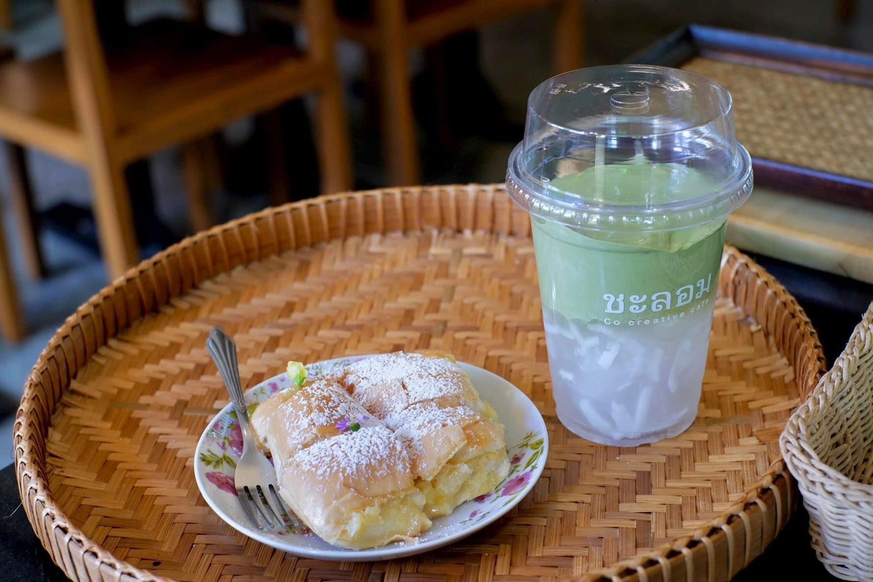 A plate of food with a fork, a clear plastic cup with a lid, and a woven basket on a woven mat.
