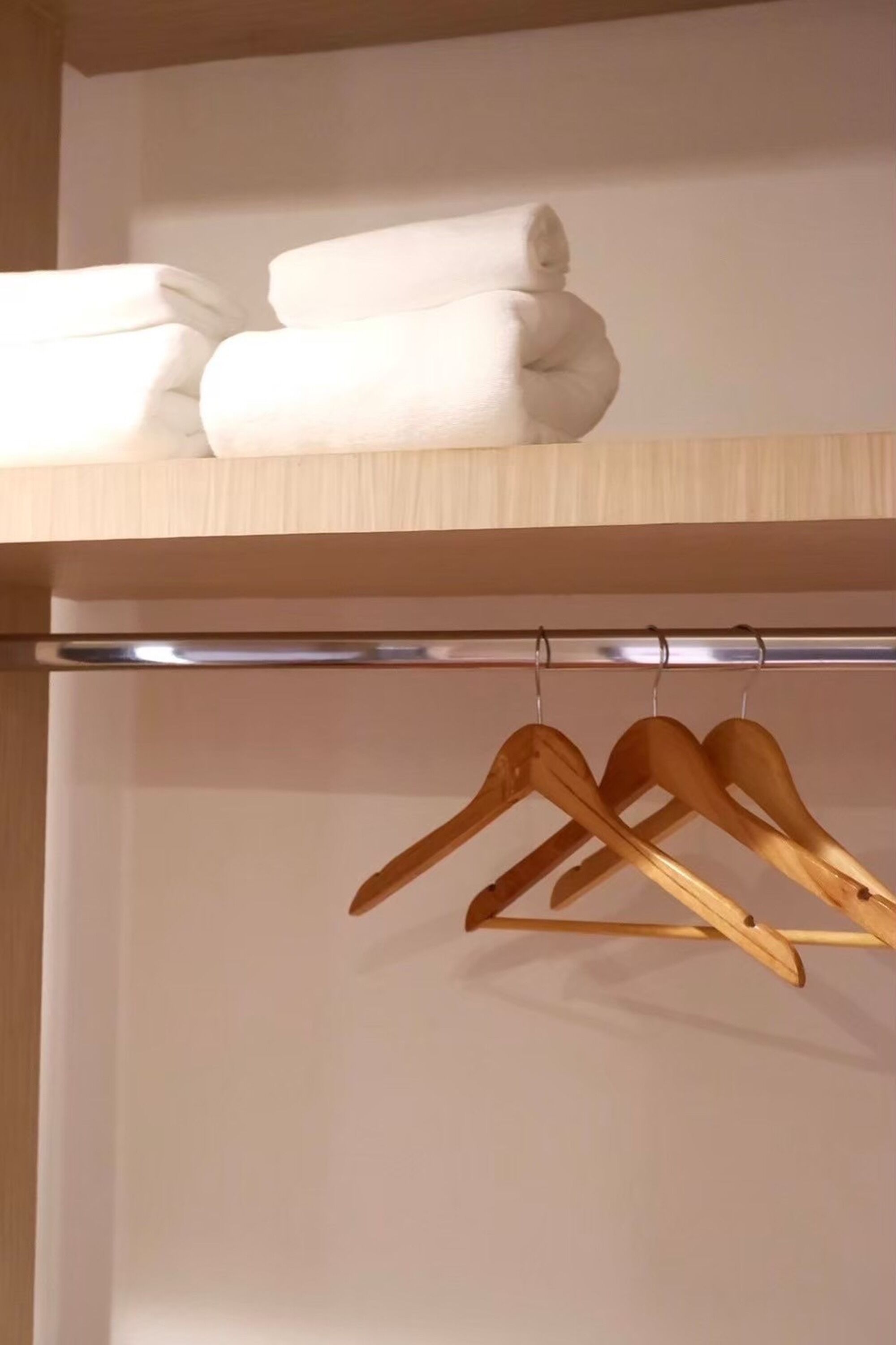 A wooden hanger rack with folded white towels on a shelf above.