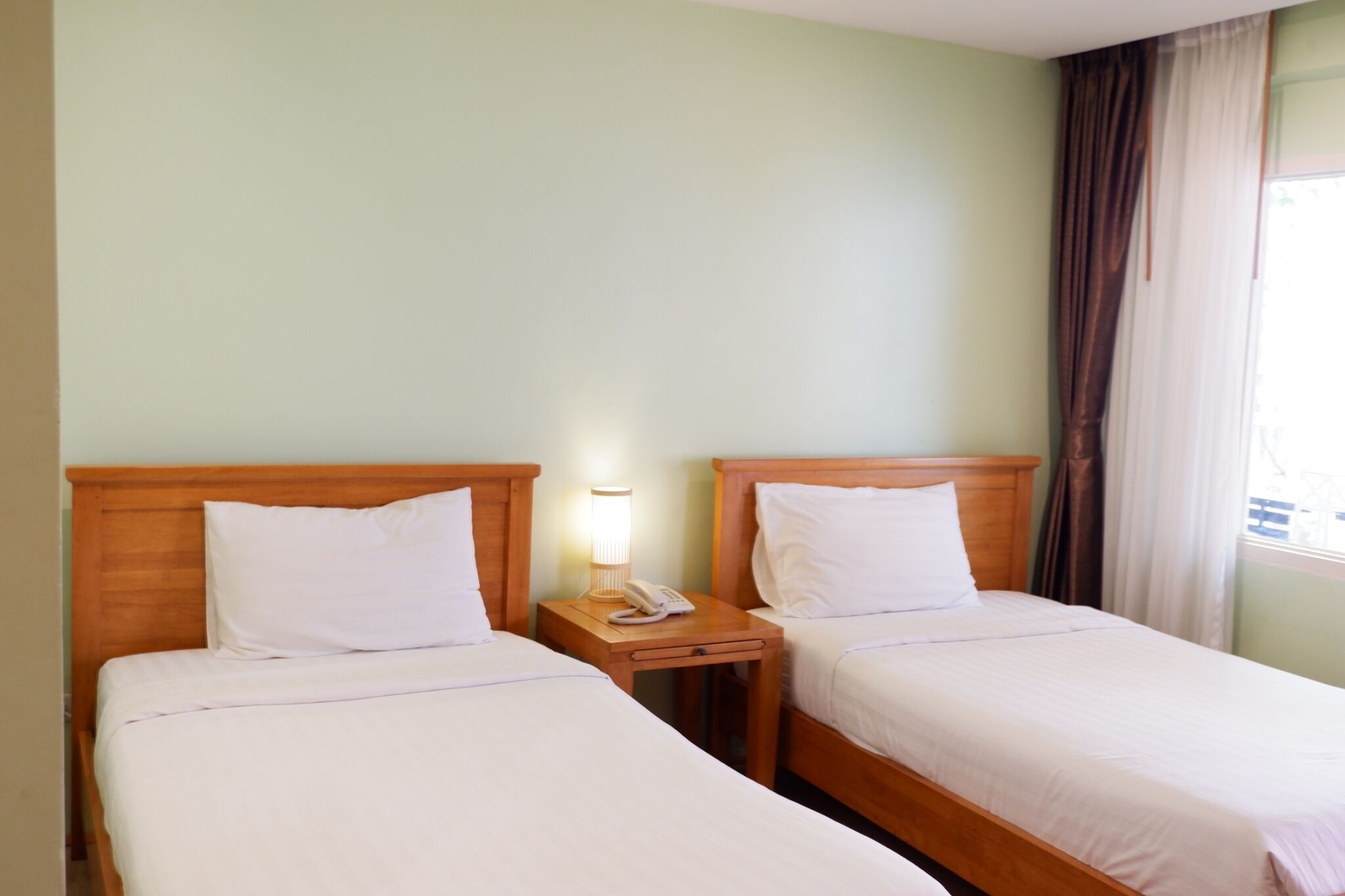 Two single beds with wooden headboards, a bedside table with a lamp, and a telephone.