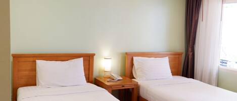 Two single beds with wooden headboards, a bedside table with a lamp, and a telephone.