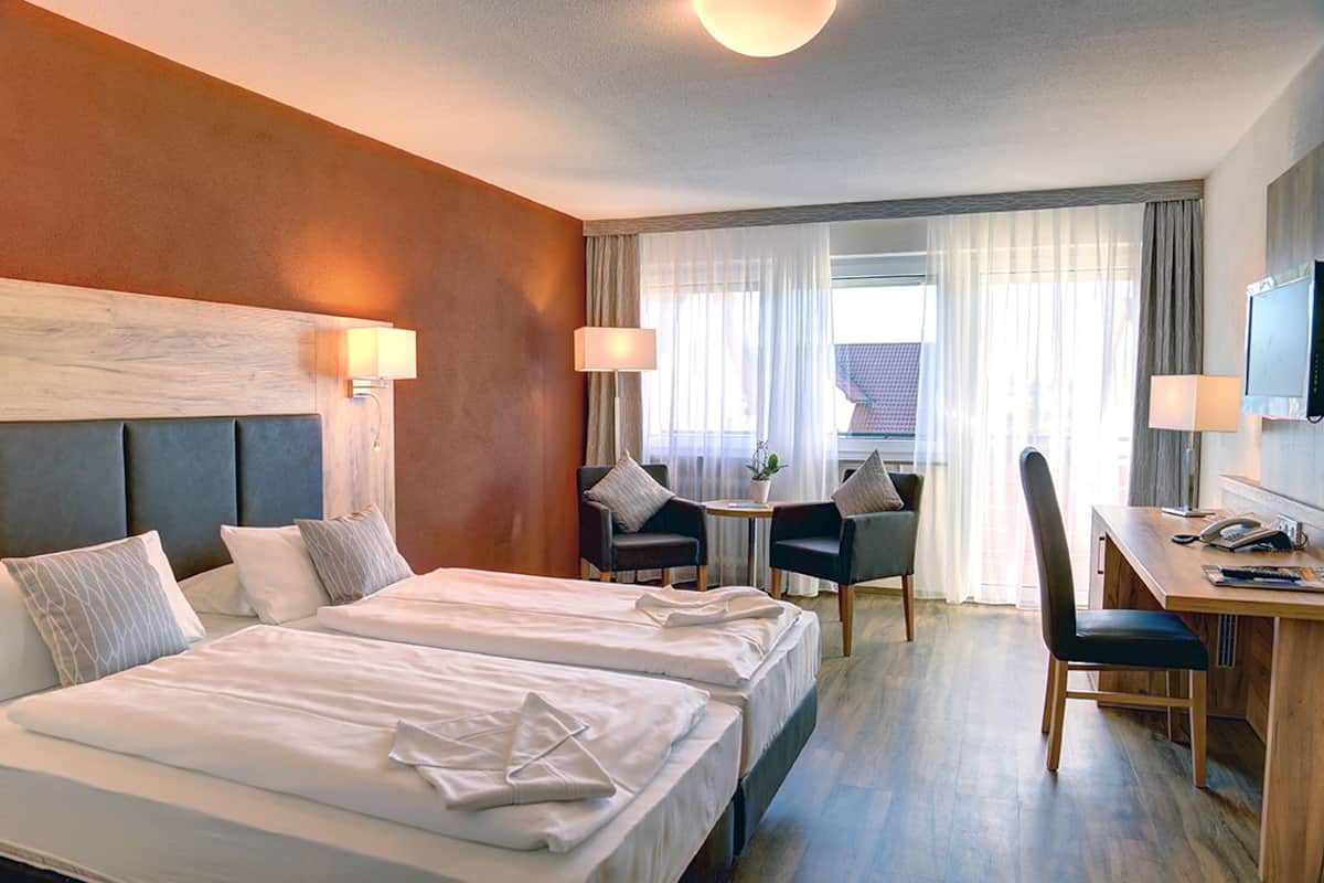 A hotel room with two beds, a desk, a chair, and a TV.