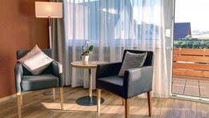 A modern hotel room with two leather armchairs, a small round table with a potted plant, and a large window with sheer curtains.