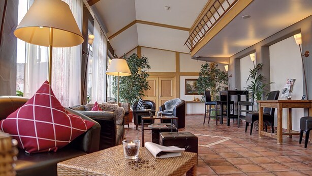 A spacious lobby with a high ceiling, a staircase, and a seating area with sofas and chairs.