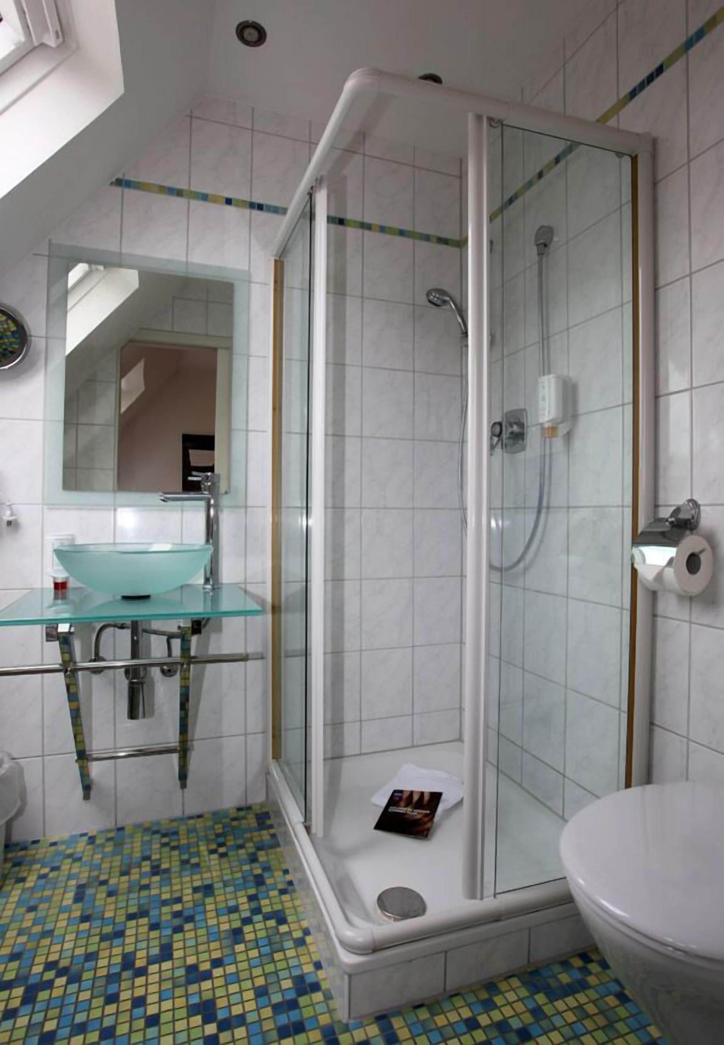 A bathroom with a glass shower enclosure, a glass sink, and a toilet.