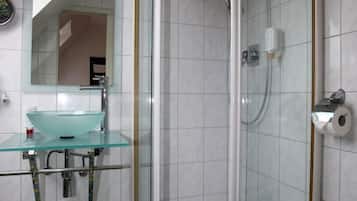 A bathroom with a glass shower enclosure, a glass sink, and a toilet.