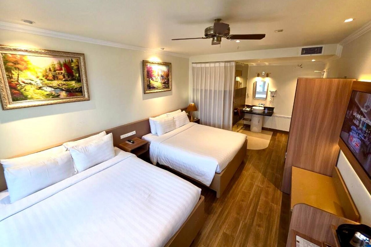A hotel room with two beds, a desk, a chair, and a television.