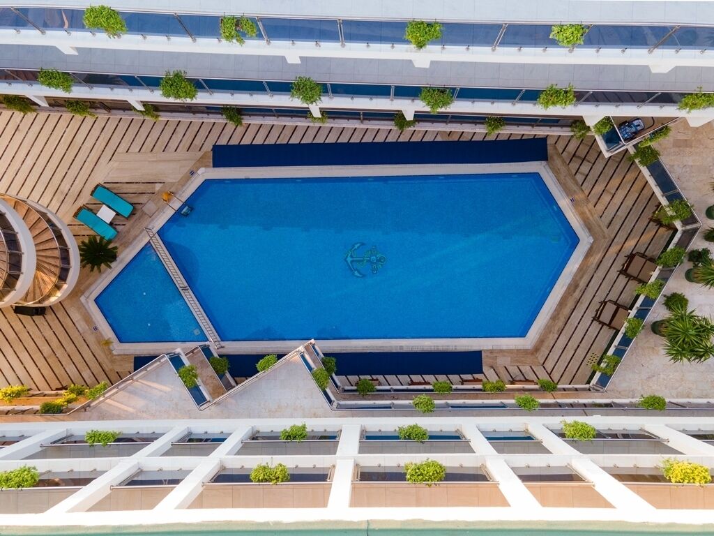 Luchtbeeld van een zwembad met een ligbed, omringd door een terras met planten en een overdekt gedeelte.