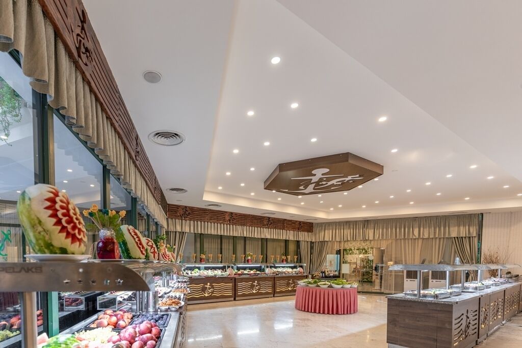 Un espace buffet comprenant différents postes de service pour les aliments, un comptoir central où les plats sont présentés, et un plafond décoratif orné d’un logo.