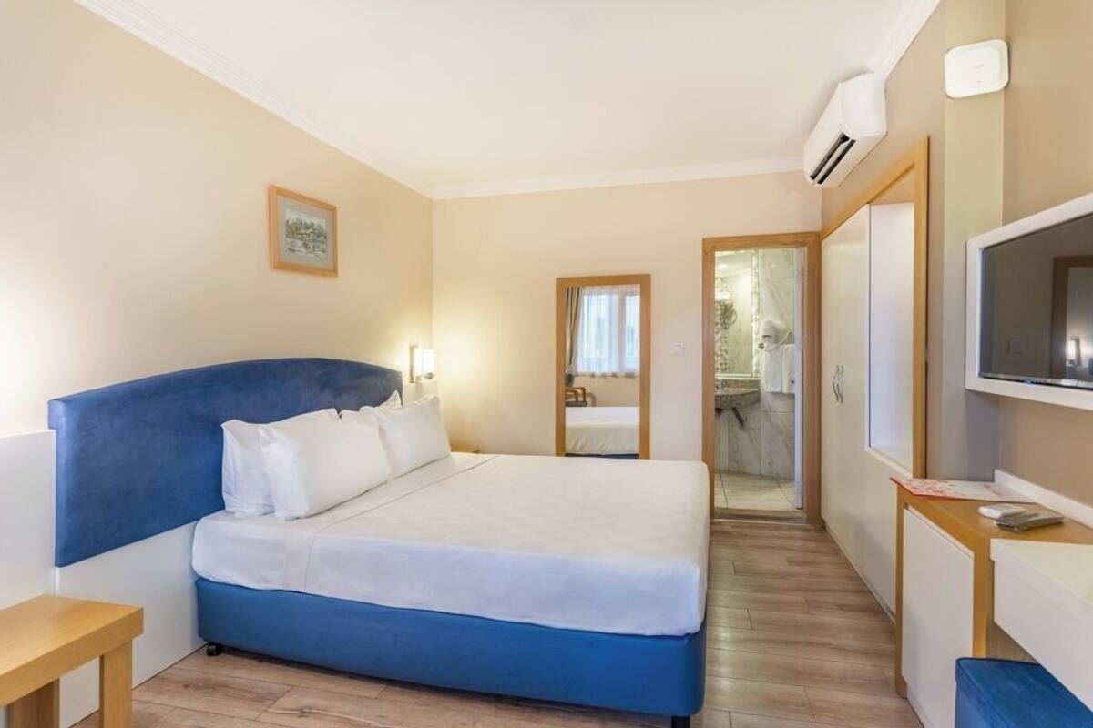 A hotel room with a bed, a TV, a desk, and a bathroom visible through an open door.