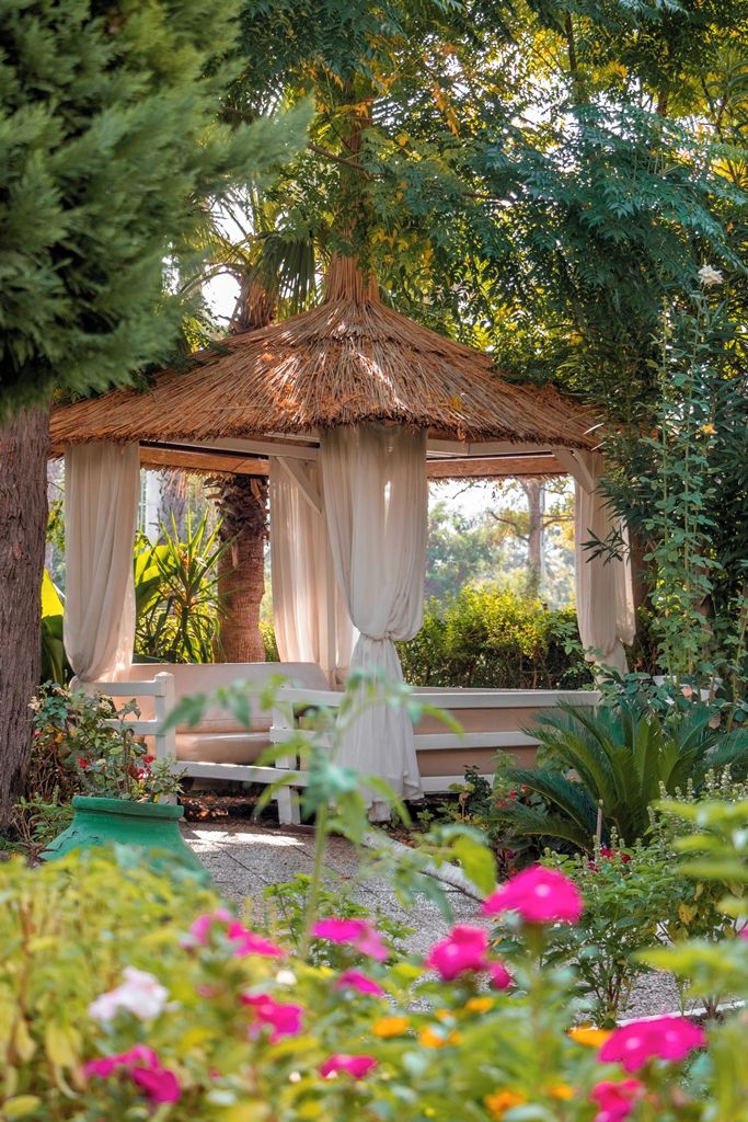 A gazebo with a thatched roof, draped curtains, and a bench.