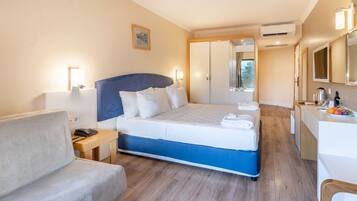 A hotel room with a bed, a desk, a chair, a bedside table, and an air conditioning unit.