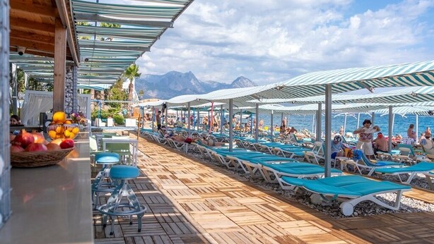 A beachside resort with sun loungers under striped canopies, a wooden deck, and a mountain backdrop. - L'ancora Beach Hotel (Kemer)