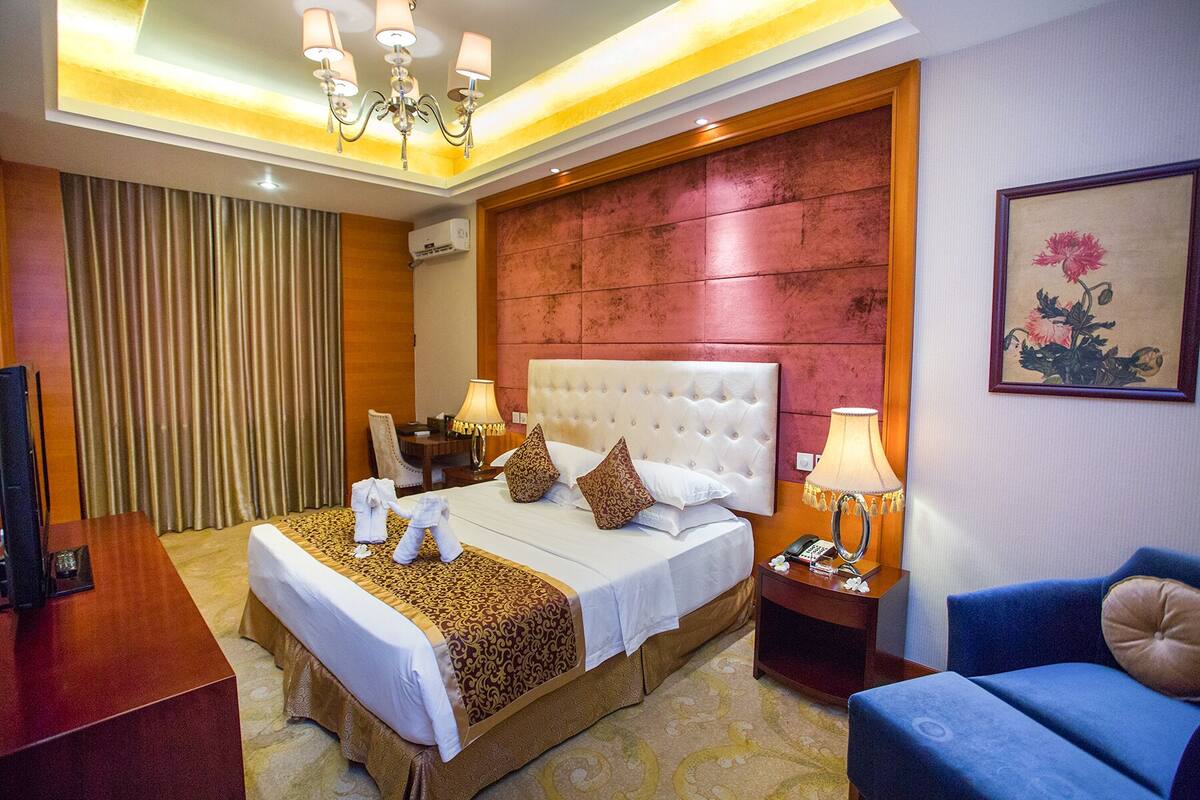 A hotel room with a large bed, a desk, a chair, a TV, and a painting on the wall.