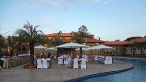 Uma área à beira da piscina com mesas, cadeiras, guarda-sóis e um deck de madeira.