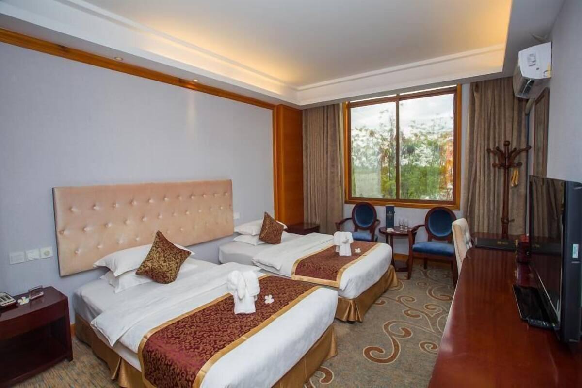 A hotel room with two beds, a desk, a chair, and a large window.