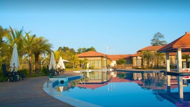 Uma área de piscina com deck de madeira, cadeiras de descanso e guarda-sóis.