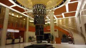 Um hall com uma coluna central, uma escadaria e um balcão de recepção.