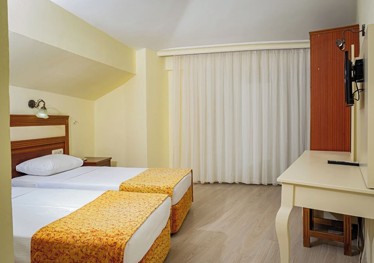 Ein Hotelzimmer mit zwei Betten, einem Schreibtisch, einem Spiegel und einem fensterbepflanzten Fenster.