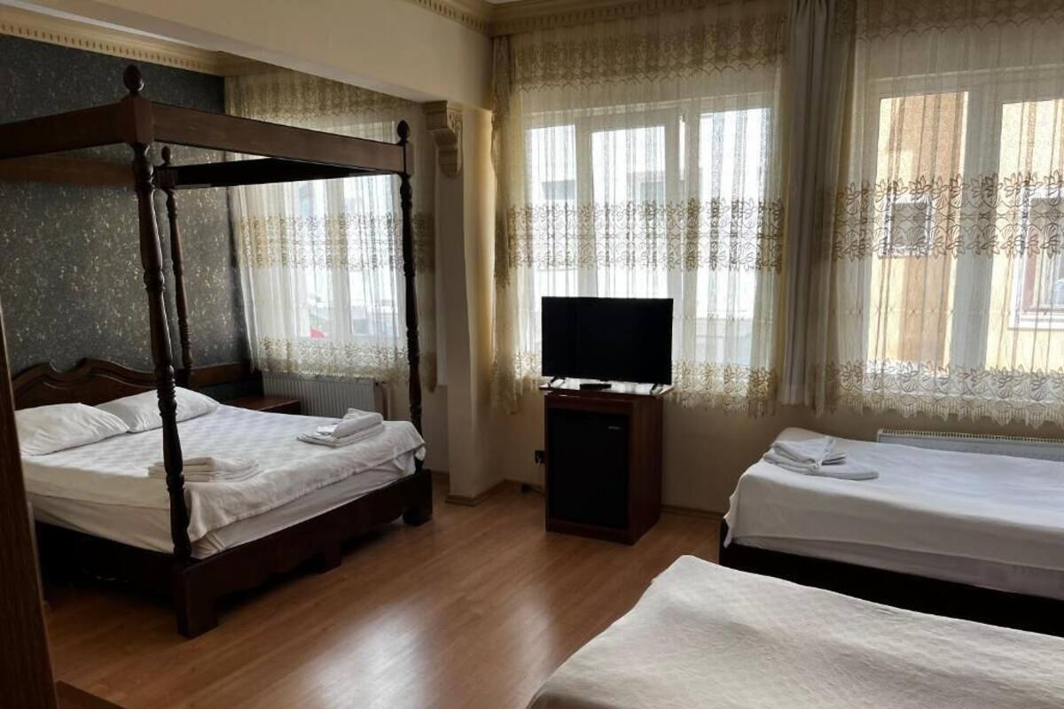 A hotel room with a four-poster bed, a single bed, a television on a stand, and a window with curtains.