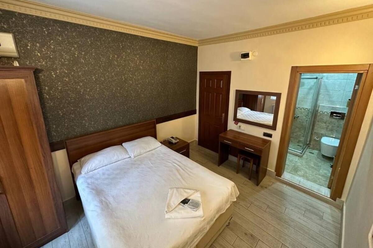 A hotel room with a bed, a desk, a wardrobe, and a bathroom visible through an open door.