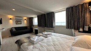 Een hotelkamer met een groot bed, een bank, een kleintje tafeltje en uitzicht op zee.