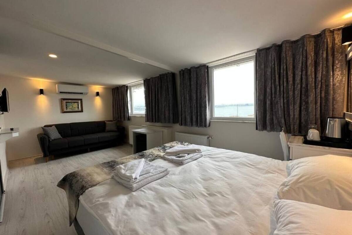 A hotel room with a large bed, a sofa, a small table, and a view of the sea.
