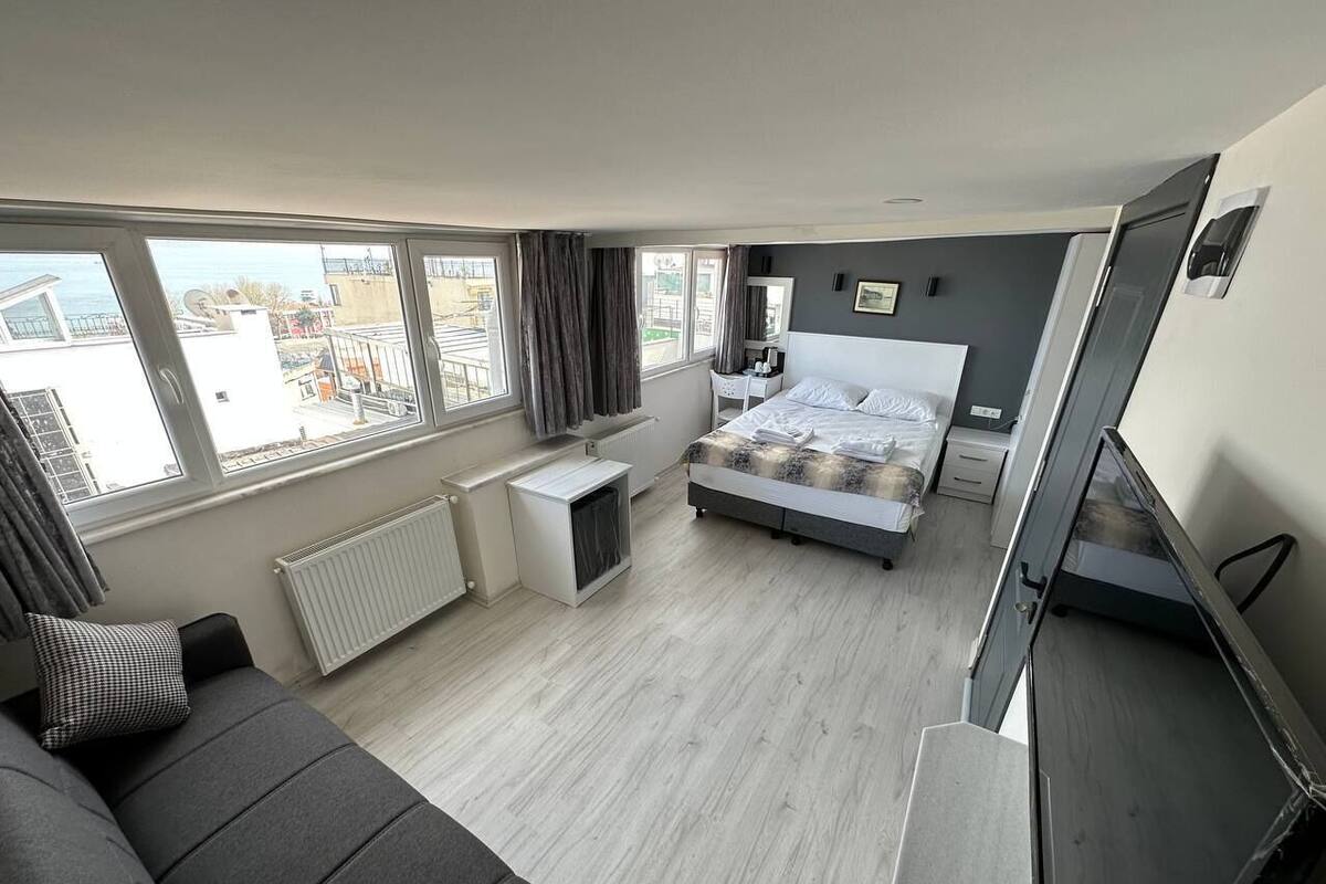 A modern hotel room with a bed, a sofa, a desk, and a view of the city.