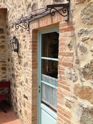 A stone building with a light blue door, a white window with a white curtain, and a black metal lantern on the wall. - Il Borghetto Andrea Tafi (Lamporecchio)
