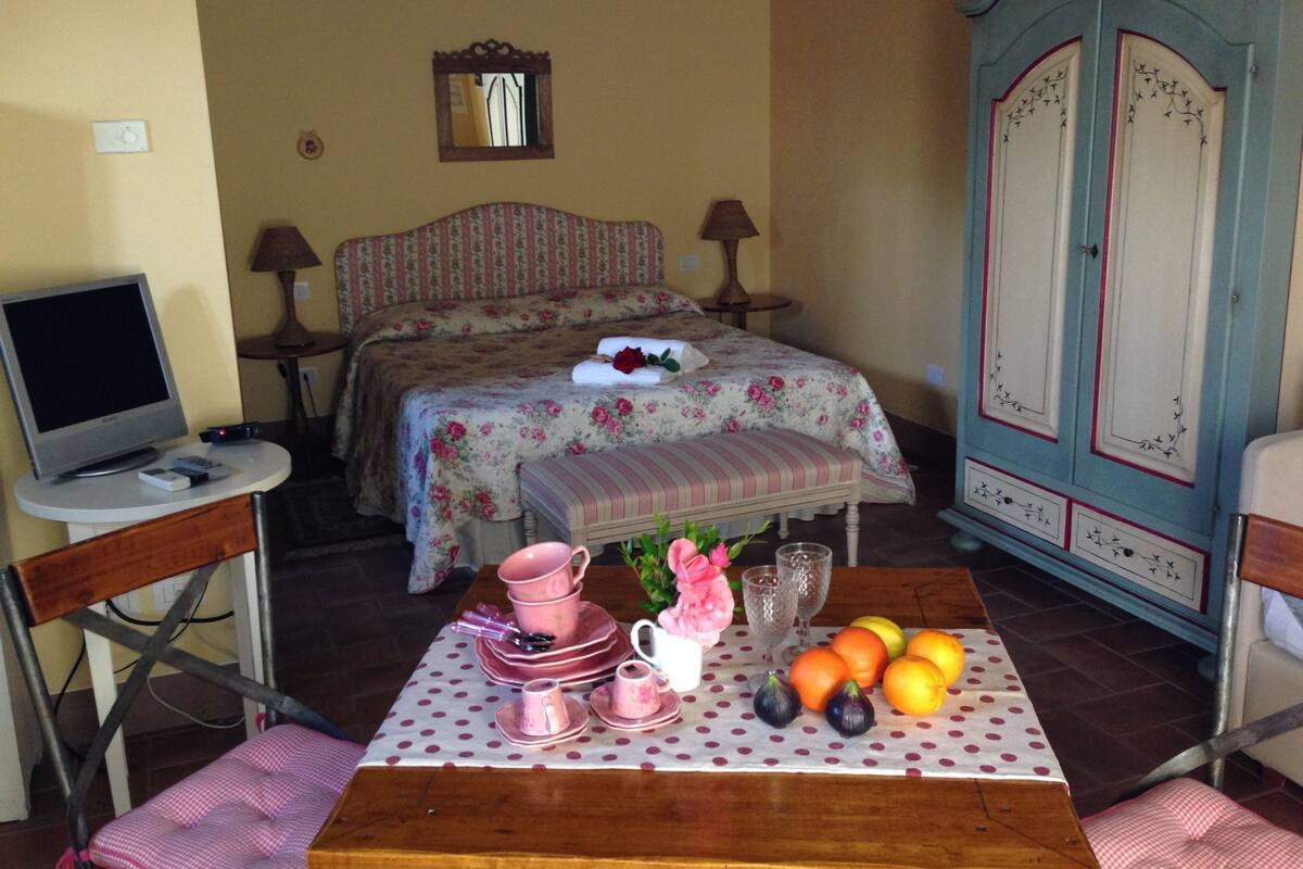 A bedroom with a bed, bedside tables, a TV, a dining table with fruit and tea sets, and a wardrobe.