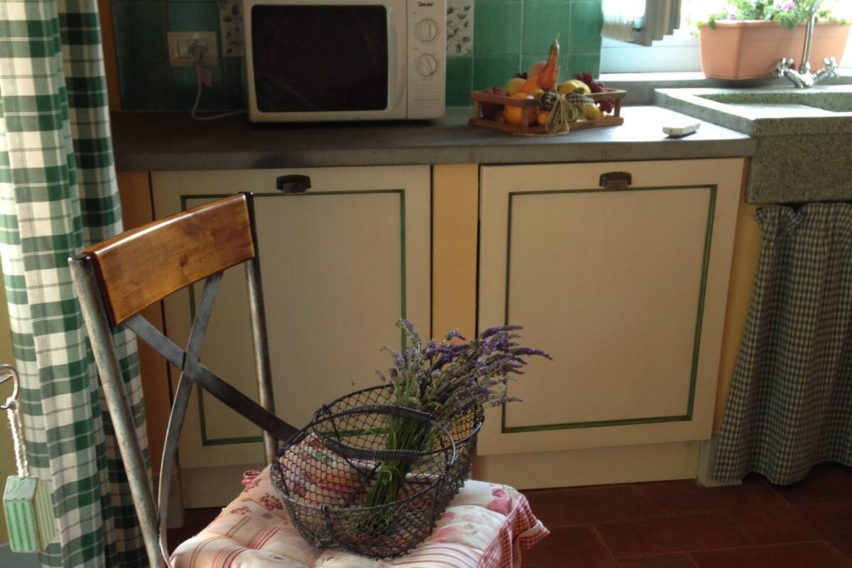 A kitchen with a microwave, a chair with a basket of flowers, and a checkered tablecloth.