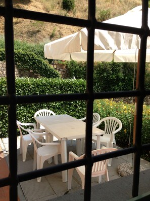 A patio area with white plastic chairs and tables, an umbrella, and a stone wall in the background. - Il Borghetto Andrea Tafi (Lamporecchio)