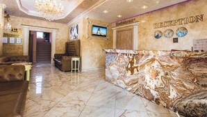 A lobby with a marble reception desk, a chandelier, a staircase, and a framed picture on the wall. - Avenue Deluxe (Sunny Beach)
