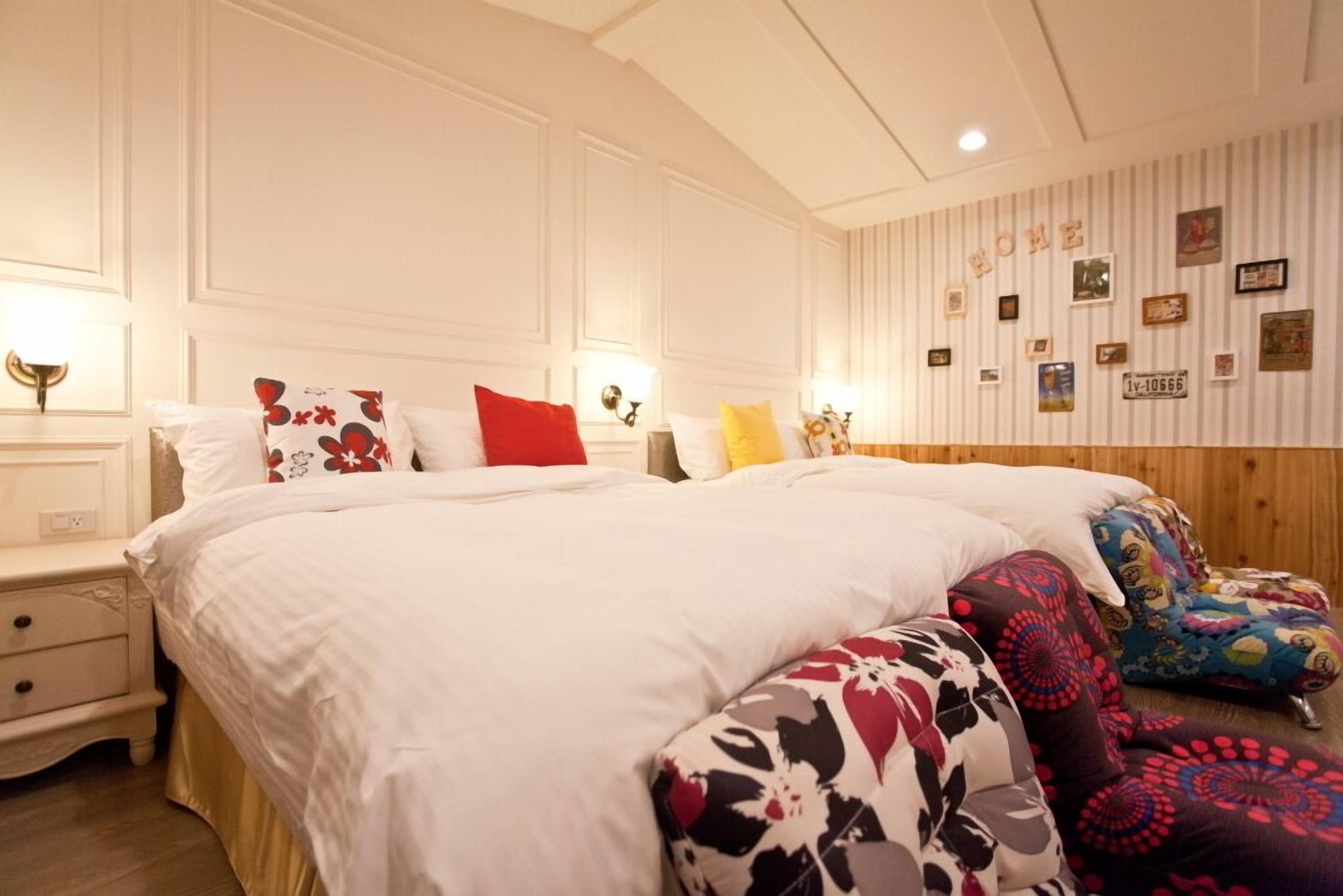 Un dormitorio con una cama grande, varios almohadones, una mesita de noche y una pared decorada con cuadros y un cartel.