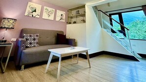 Un soggiorno moderno con divano, tavolino e opere d'arte alle pareti. Una scala conduce a un piano superiore con vista sull'esterno.