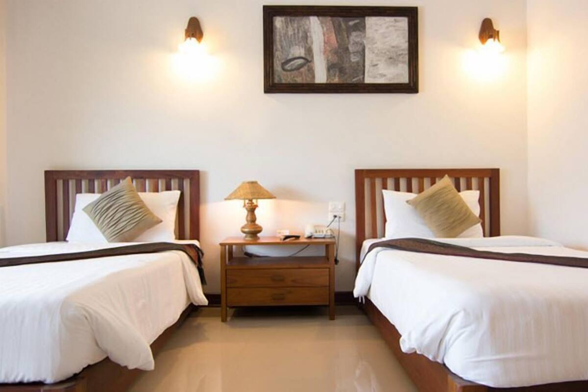 Une chambre d’hôtel avec deux lits simples, une table de chevet avec une lampe et un tableau au mur.