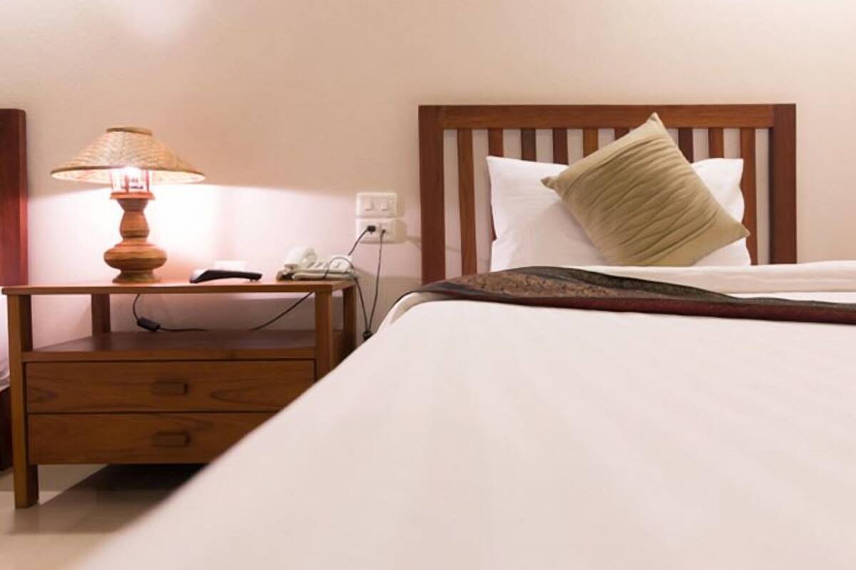 Un lit bien fait, avec une tête de lit en bois, une lampe de chevet et une table de chevet sur laquelle se trouvent un téléphone et une lampe.