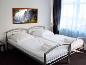 A single bed with metal frame and white bedding in a room with a painting of a waterfall on the wall.
