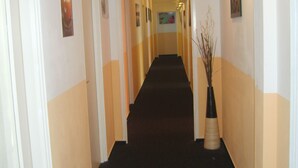 En hotellkorridor med svart matta, vita väggar och en klocka på väggen.