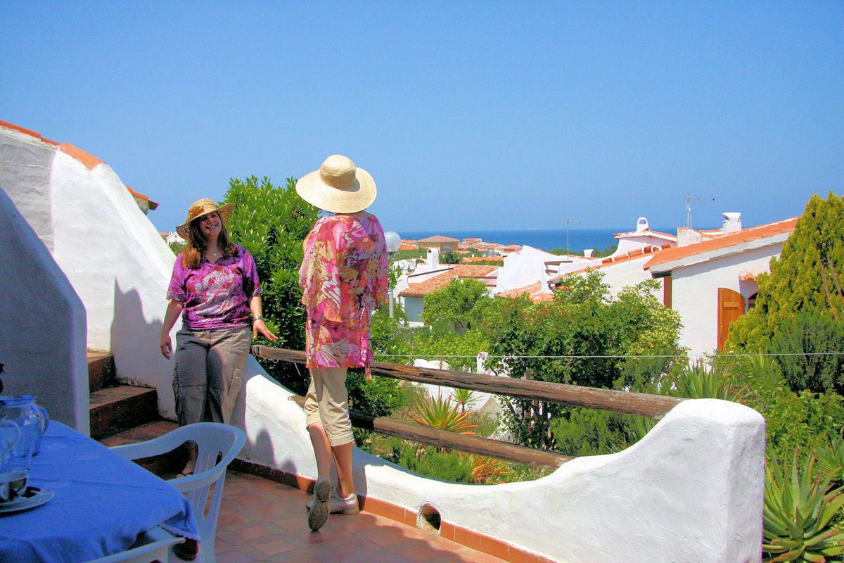 A terrace with white walls, a table with chairs, and a view of buildings and the sea.