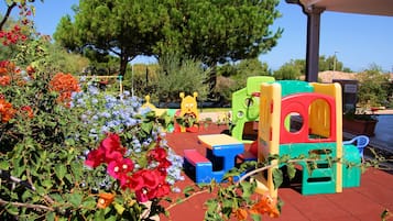 Children can play on the slide and climbing elements in this outdoor play area surrounded by lush gardens and a serene lake.