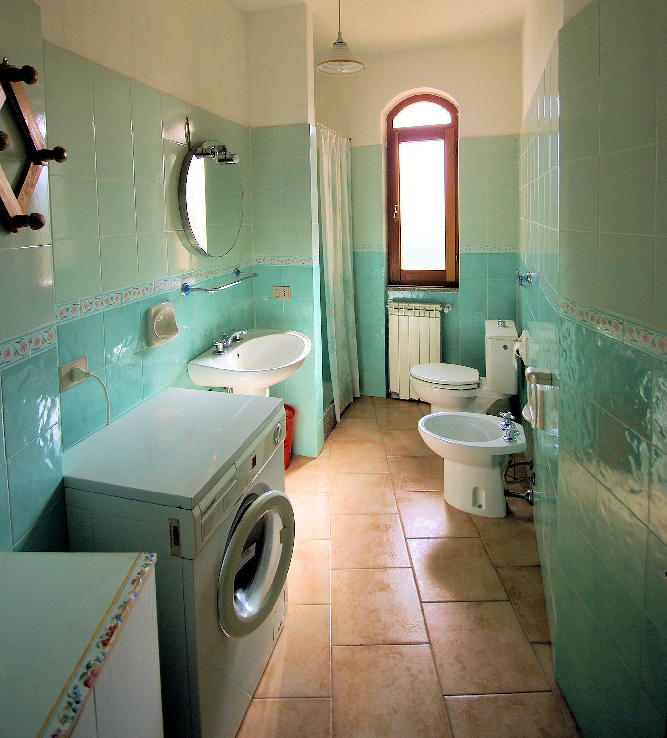 A compact bathroom with a washing machine, two sinks, a toilet, and a bidet.