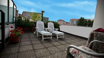 Ein Balkon mit zwei weißen Liegestühlen und einem Topf mit roten Blüten.