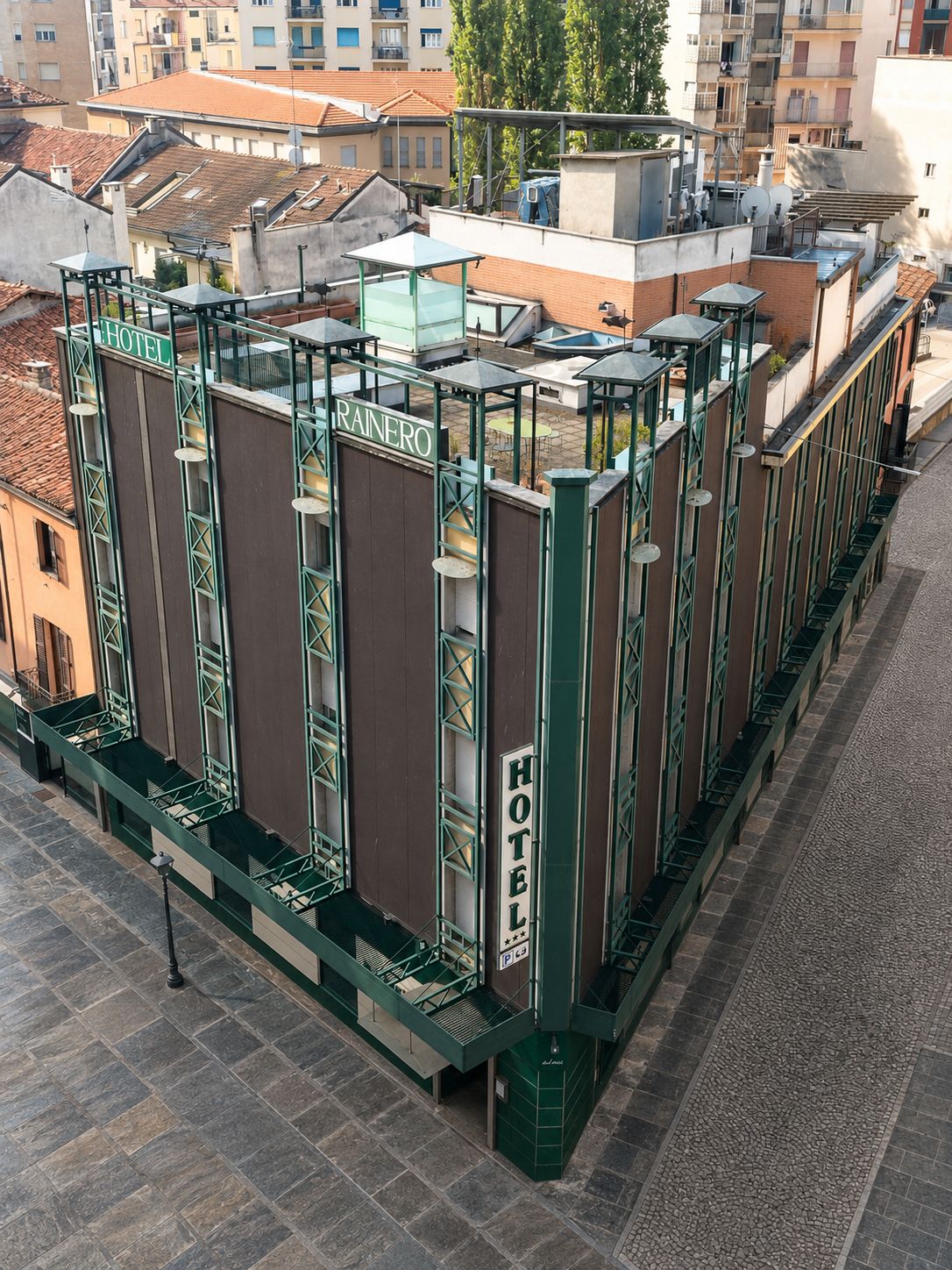 Un hôtel avec une enseigne «HÔTEL» bien visible, un espace extérieur abrité et une vue sur les bâtiments environnants.