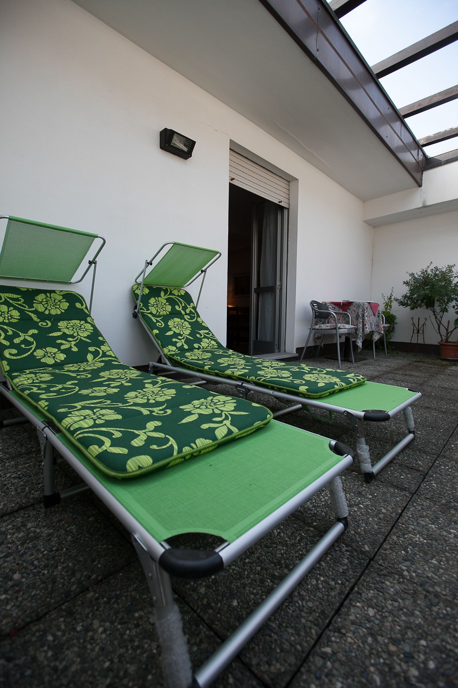 Two green lounge chairs with floral patterns, a table with a red tablecloth, and a potted plant.
