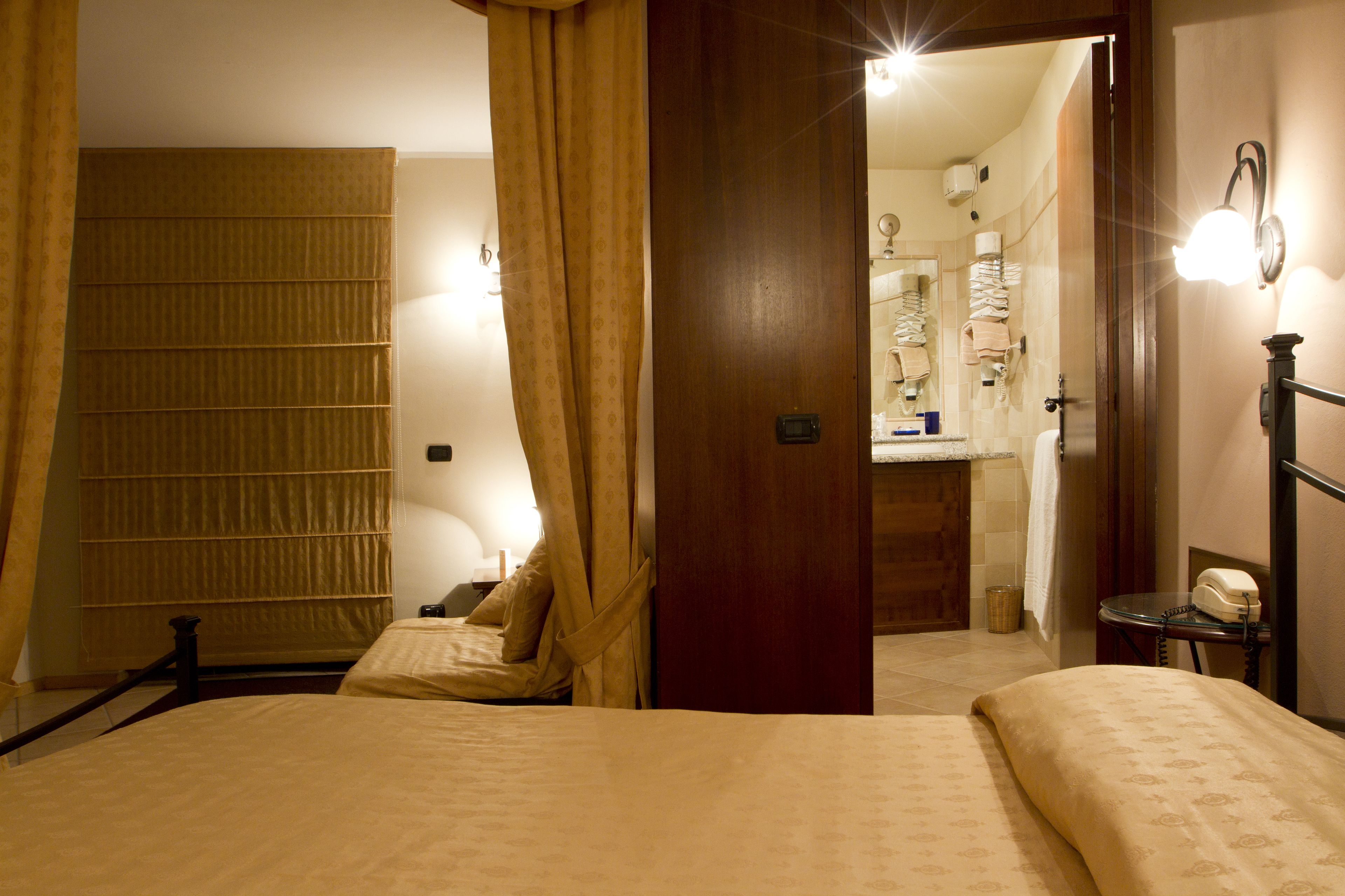 Een hotelkamer met een bed, nachtkastje, spiegel en een badkamer die door een open deur zichtbaar is.