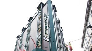 Un hotel con fachada verde, entrada visible y un letrero que indica que es un hotel.